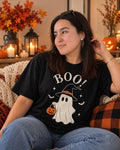 Woman wearing a black t-shirt printed with BOO and a ghost in a witch hat holding a pumpkin bucket