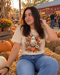 Woman wearing a cream t-shirt printed with a ghost surrounded by autumn flowers at a pumpkin patch