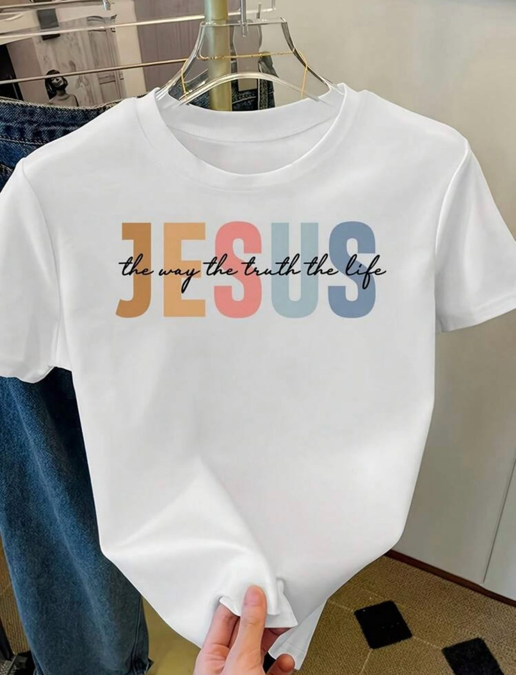White t-shirt on a hanger printed with JESUS in colorful letters and the way the truth the life