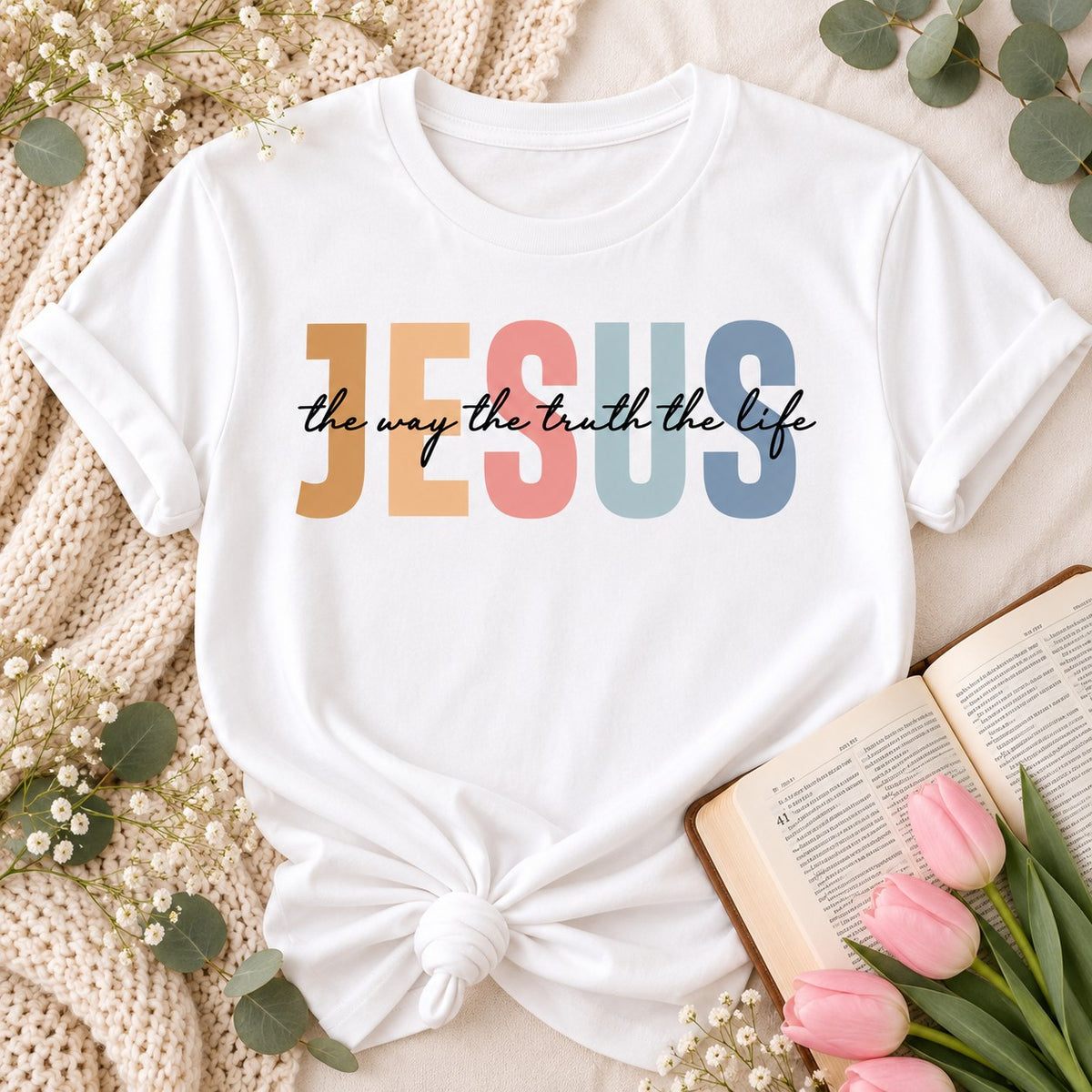 White t-shirt flat lay printed with JESUS in colorful letters and the way the truth the life, with a Bible and tulips