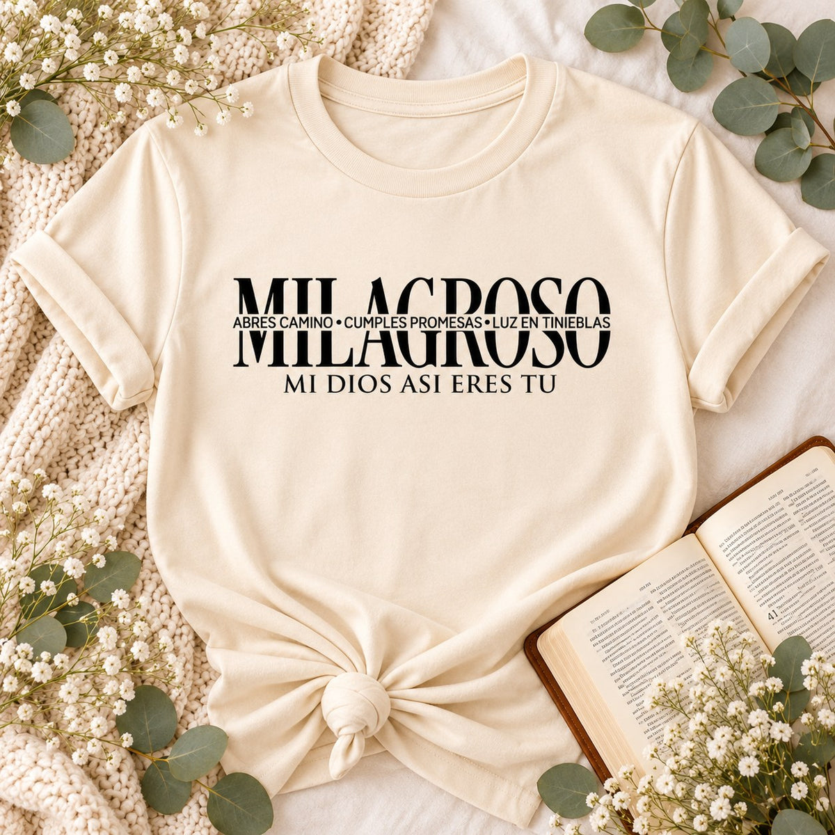 Cream t-shirt flat lay printed with MILAGROSO and Mi Dios así eres tú, next to an open Bible