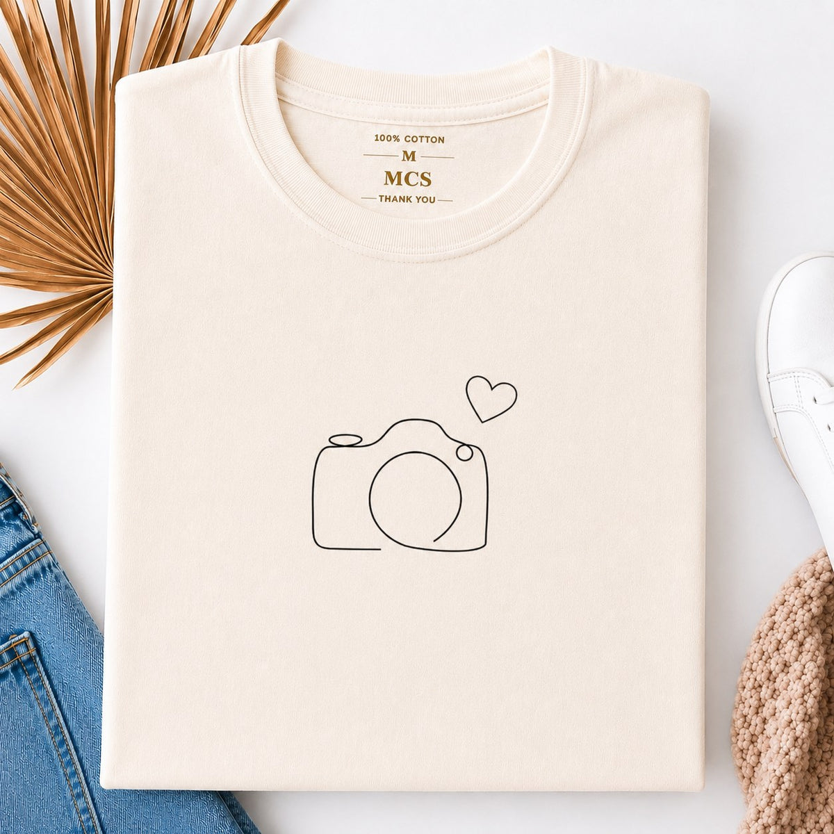Cream t-shirt with a minimalist line-drawn camera and a small heart