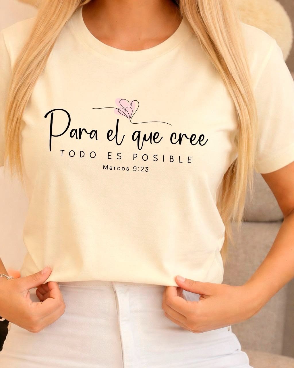 Woman wearing a cream t-shirt printed with Para el que cree, todo es posible and a pink heart