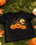 Black kids Halloween t-shirt with grinning pumpkins, one in a witch hat, with bats and a full moon